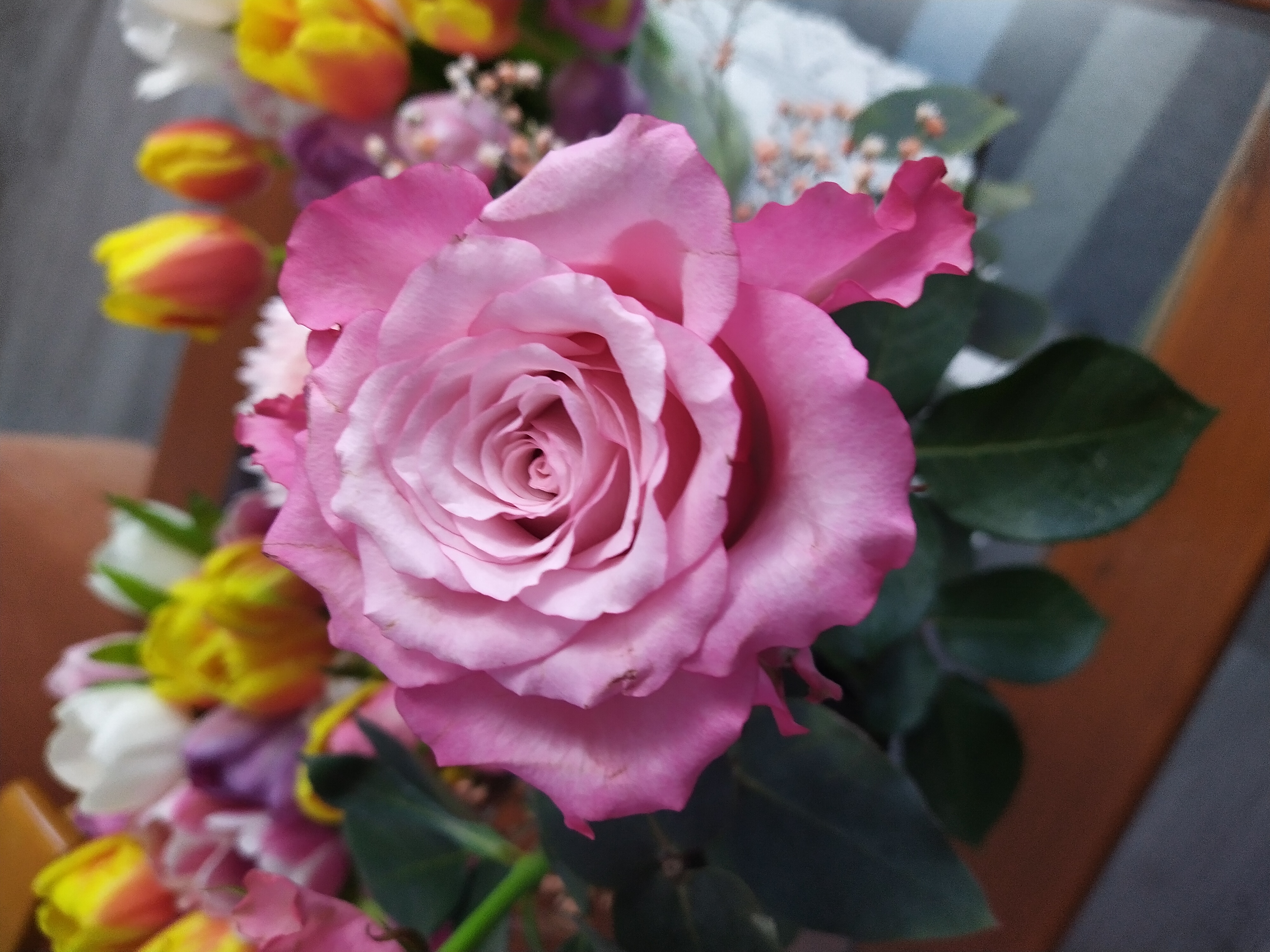 kukkia maljakossa, päänä esillä vaaleanpunainen iso ruusu.